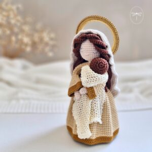 Nossa Senhora em amigurumi de crochê com vestido bege e auréola dourada segurando o Menino Jesus