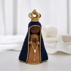 Nossa Senhora Aparecida em amigurumi com manto azul e coroa dourada, peça em crochê sobre fundo claro