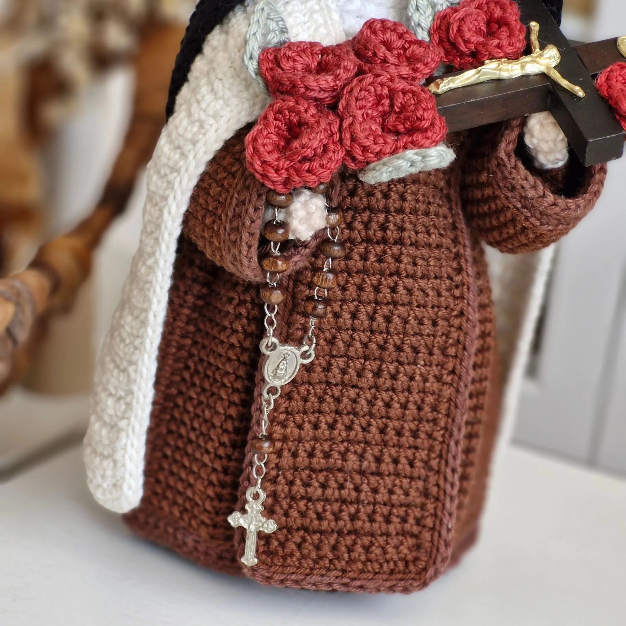 Close do rosário, do crucifixo e das rosas vermelhas da Santa Teresinha em amigurumi, destacando os detalhes e o acabamento da peça.