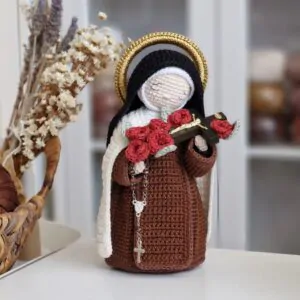 Santa Teresinha do Menino Jesus em amigurumi segurando um crucifixo com rosas vermelhas e rosário carmelita.