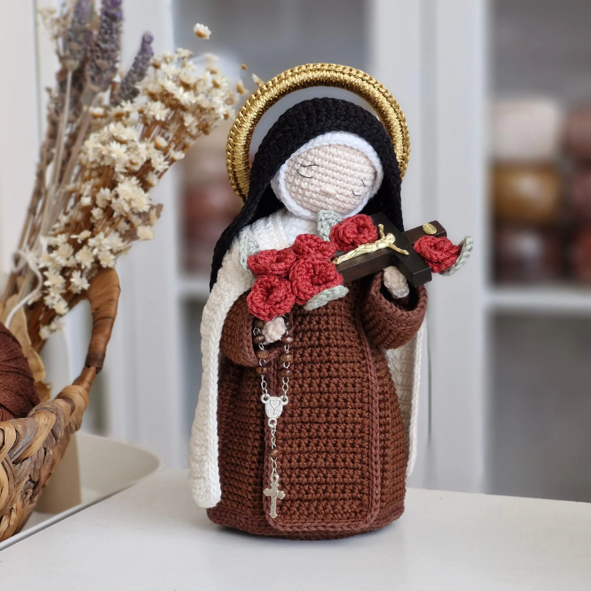 Santa Teresinha do Menino Jesus em amigurumi segurando um crucifixo com rosas vermelhas e rosário carmelita.