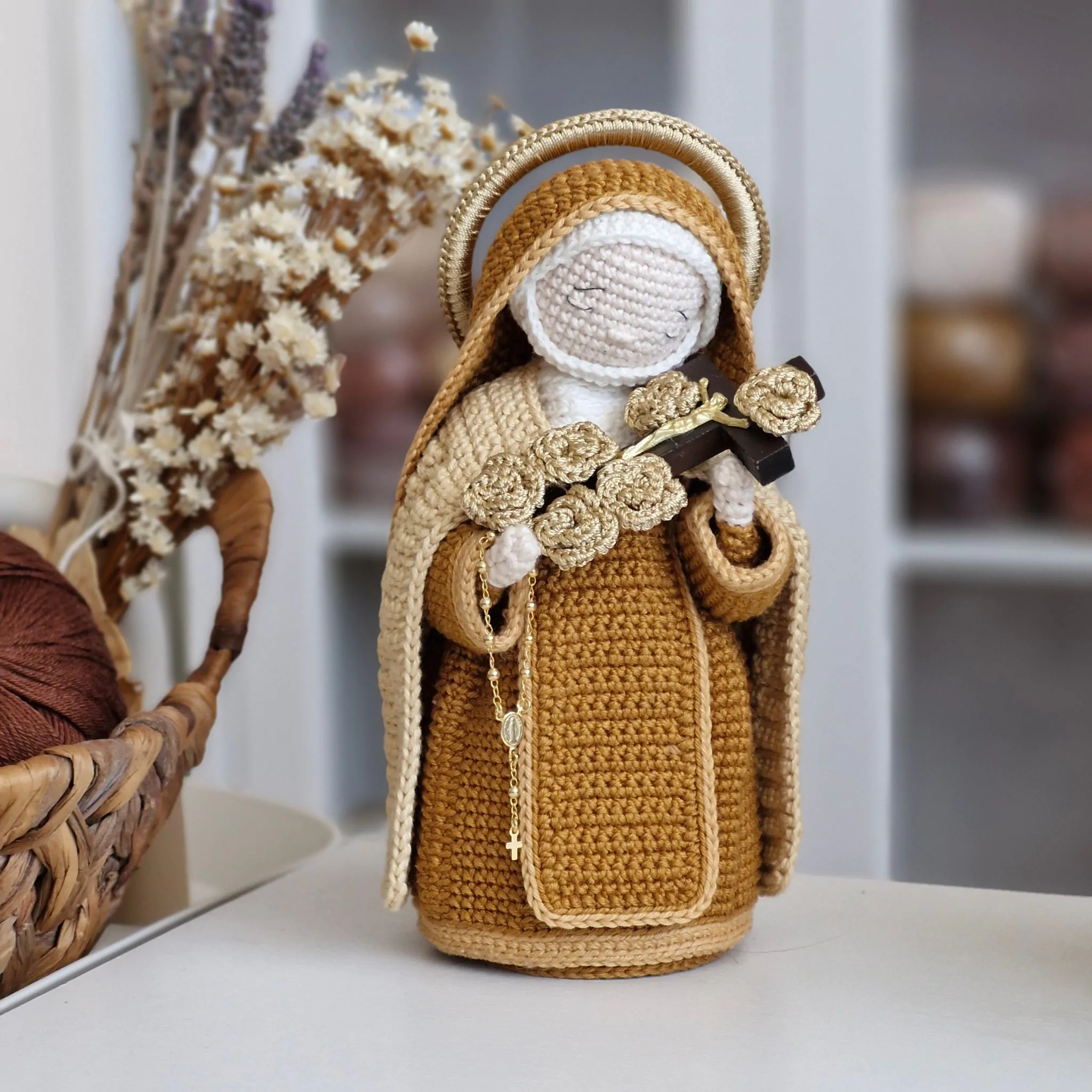 Santa Teresinha do Menino Jesus em amigurumi segurando crucifixo com rosas douradas e rosário, inspirada na iconografia carmelita.